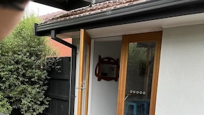 An outdoor patio area with a wooden table and benches, a small dog house, and a glass door leading to an interior space. - Ronny's Tootgarook. (Tootgarook)