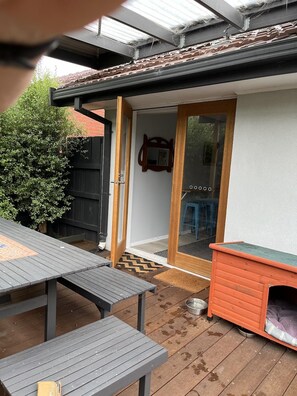 Une terrasse avec des tables de pique-nique, une niche pour chien et une porte donnant sur un espace intérieur.