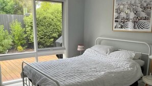 Une chambre à coucher avec un lit, un ventilateur de plafond, une fenêtre donnant sur un paysage verdoyant et un tableau encadré accroché au mur.