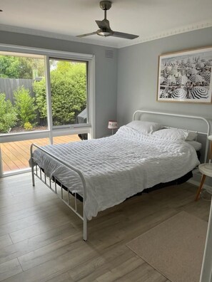 Une chambre à coucher avec un lit, un ventilateur de plafond, une fenêtre et un tableau encadré au mur.