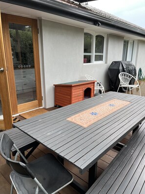 A wooden deck with a table and chairs, a small wooden structure, and a barbecue grill.
