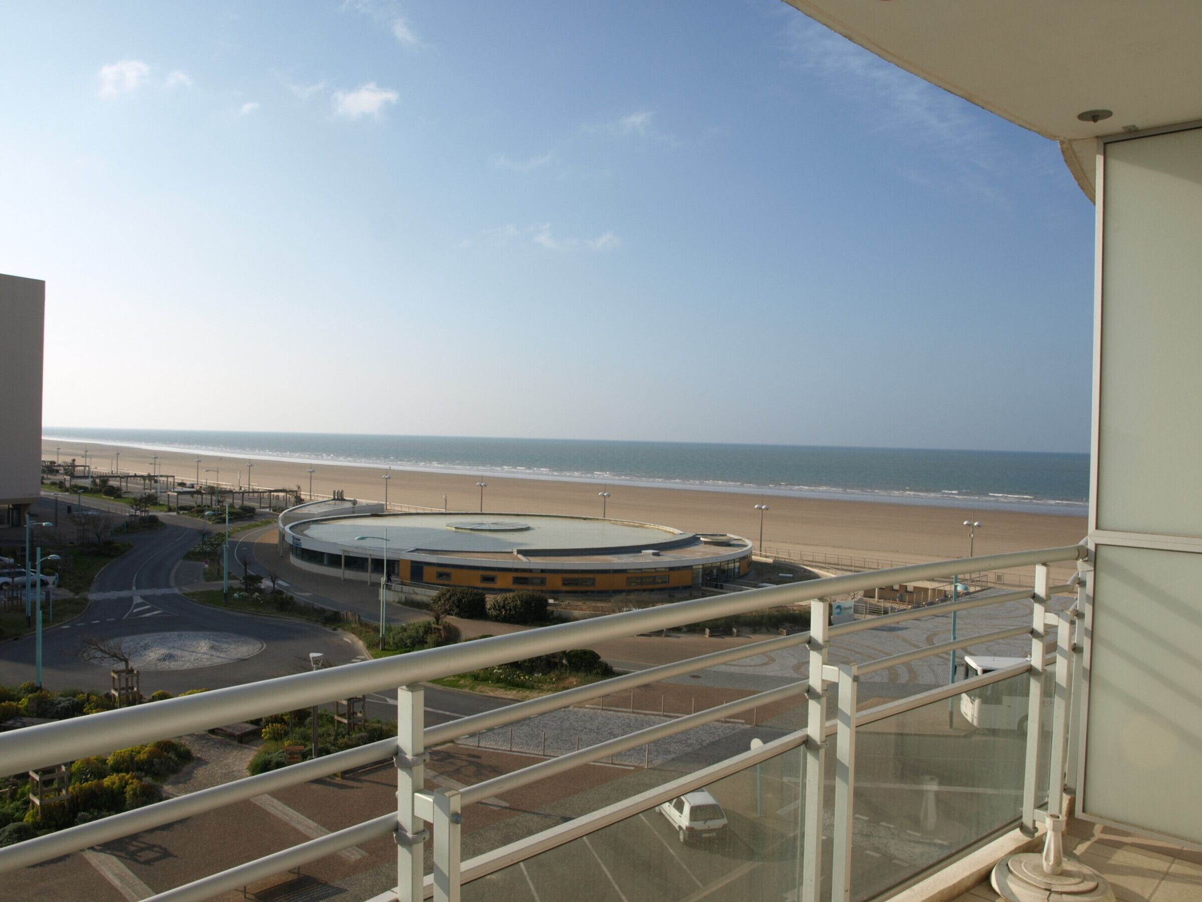 A view from a balcony overlooking a beach, a round building, and a parking area.