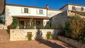 A stone building with a courtyard, featuring a stone wall, a wooden staircase, and a tiled roof.