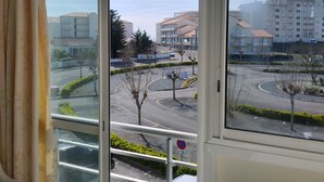A view from a window overlooking a parking area with a roundabout, buildings, and a clear sky. - Spacious apartment for 4, 200m from the beach, private parking included (Saint-Hilaire-de-Riez)