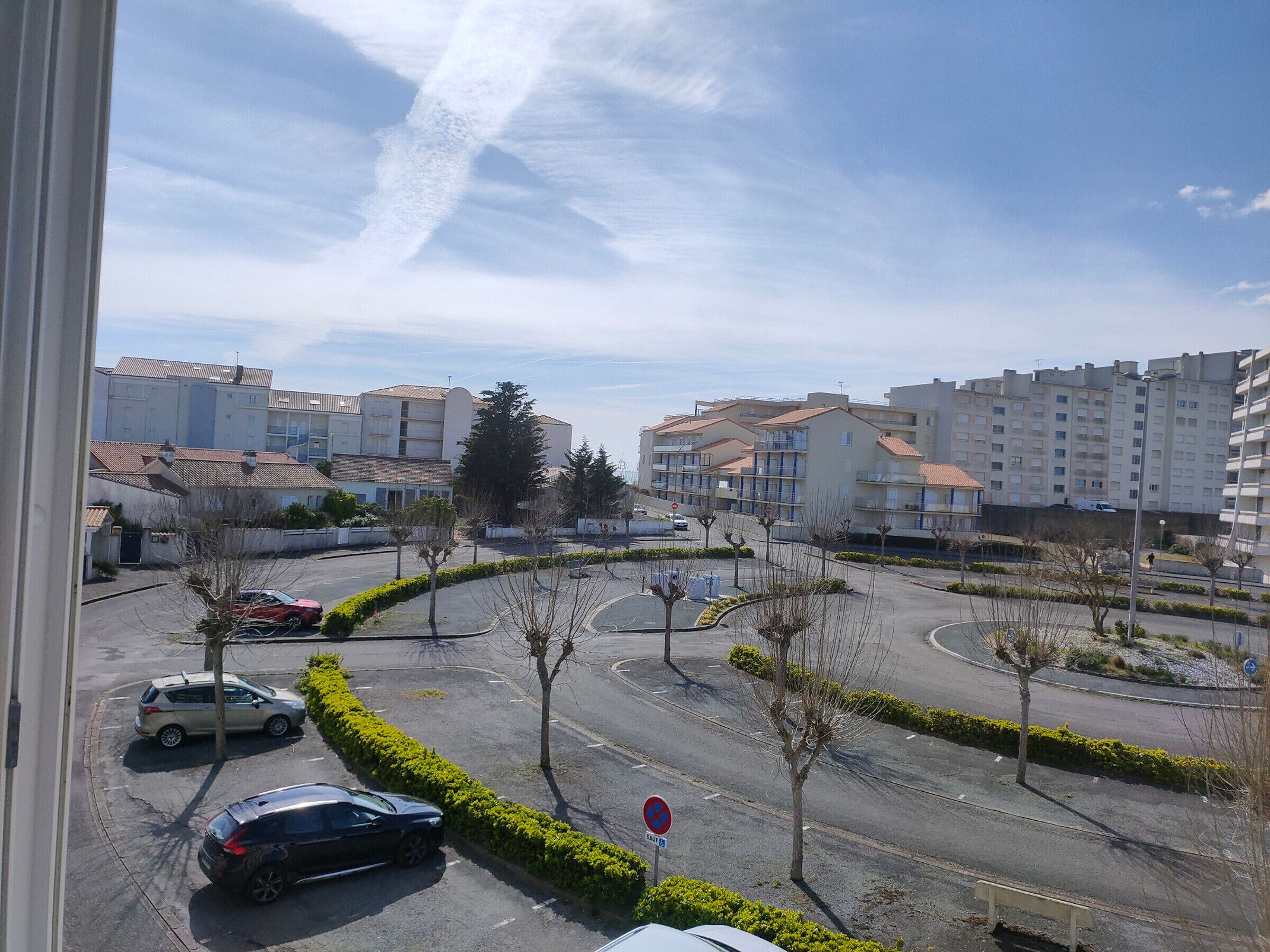 Une vue d’un quartier résidentiel avec des immeubles d’appartements, un rond-point et des voitures garées.