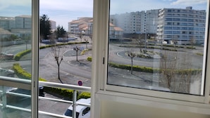 A view from a window overlooking a parking area with a roundabout, buildings in the background, and a clear sky. - Spacious apartment for 4, 200m from the beach, private parking included (Saint-Hilaire-de-Riez)
