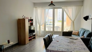 A living room with a large table, a TV, and a sofa. - Spacious apartment for 4, 200m from the beach, private parking included (Saint-Hilaire-de-Riez)