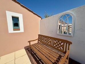 A wooden bench outside a building with a small window and a larger arched window.