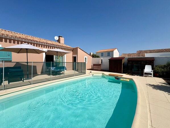A swimming pool with a clear blue water surface, surrounded by a fenced patio area with outdoor furniture.