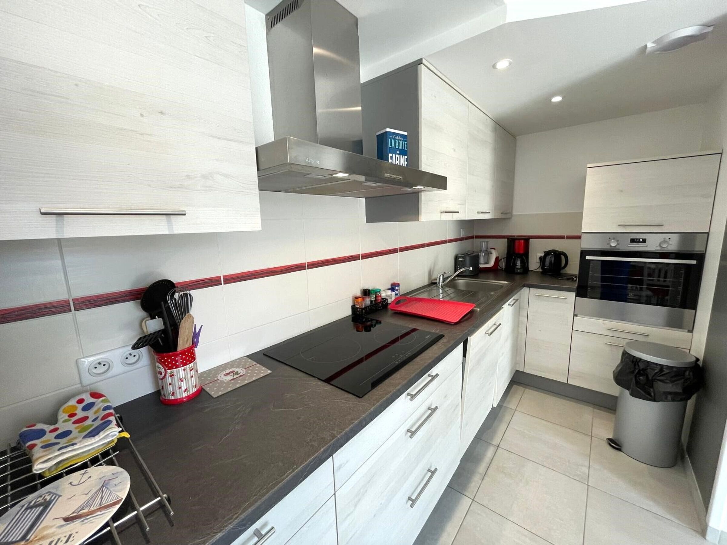 A modern kitchen with white cabinetry, a stainless steel range hood, a built-in oven, and a coffee maker.