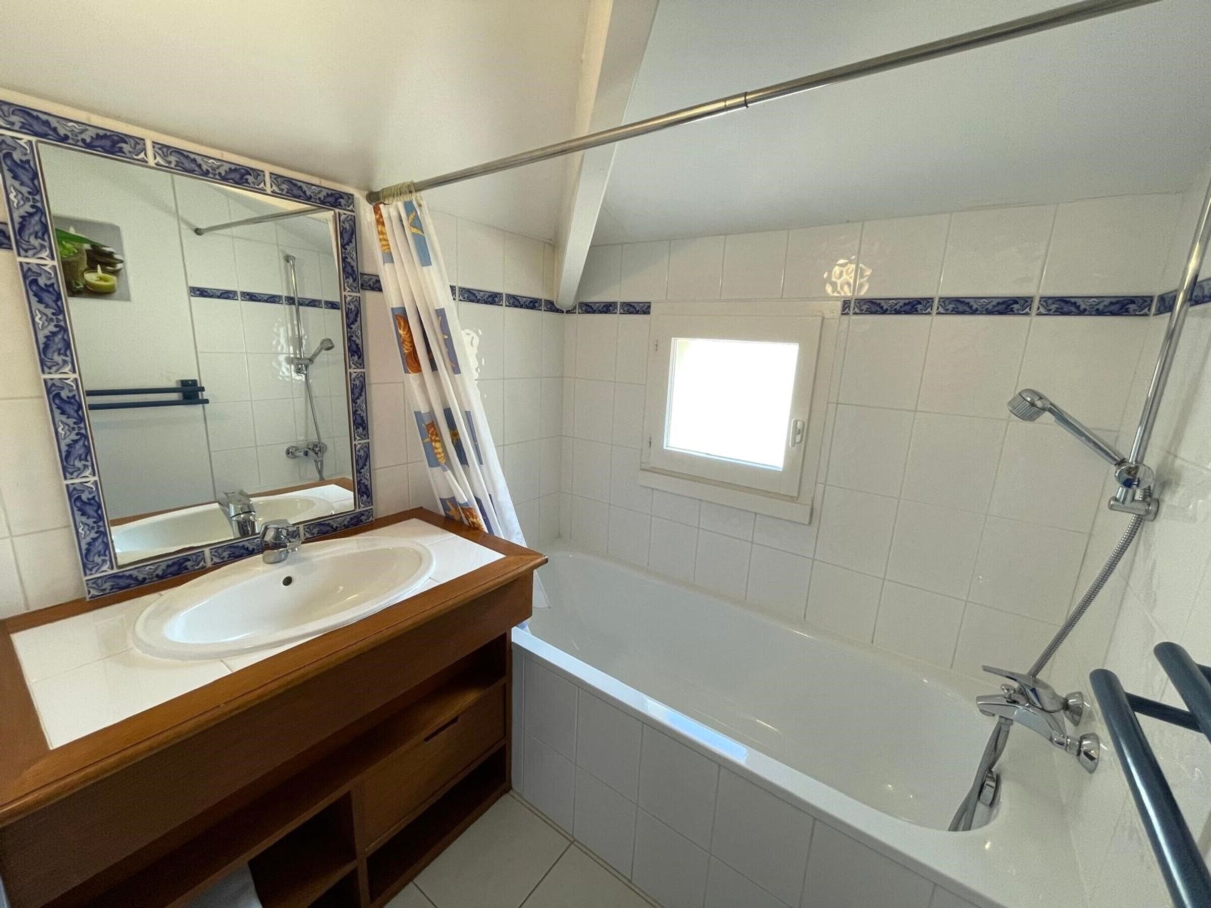 Une salle de bain avec un meuble-lavabo en bois, un grand miroir, une baignoire et un espace douche.