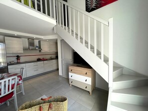 A modern kitchen with white cabinetry, a dining area with a red table and chairs, and a staircase leading to an upper level.