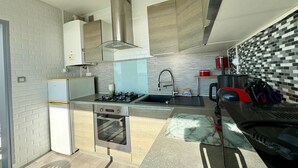 A modern kitchen with a built-in oven, gas stove, stainless steel range hood, and a tiled backsplash. - Bright studio with alcove, sea-view balcony, private parking (Saint-Jean-de-Monts)
