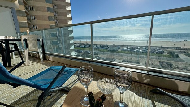 A balcony with a view of the beach, a table with two wine glasses, a chair, and a small potted plant. - Bright studio with alcove, sea-view balcony, private parking (Saint-Jean-de-Monts)