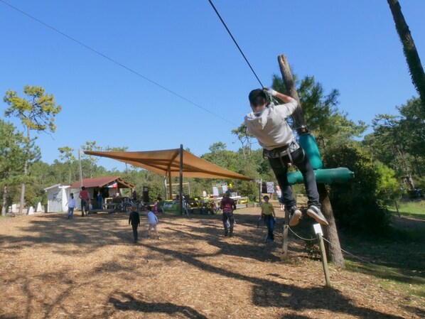 A person zip-lining with a safety harness, trees, and a shaded area in the background. - Bright studio with alcove, sea-view balcony, private parking (Saint-Jean-de-Monts)