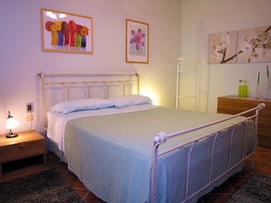 A bedroom with a bed, bedside table, lamp, and artwork on the walls.