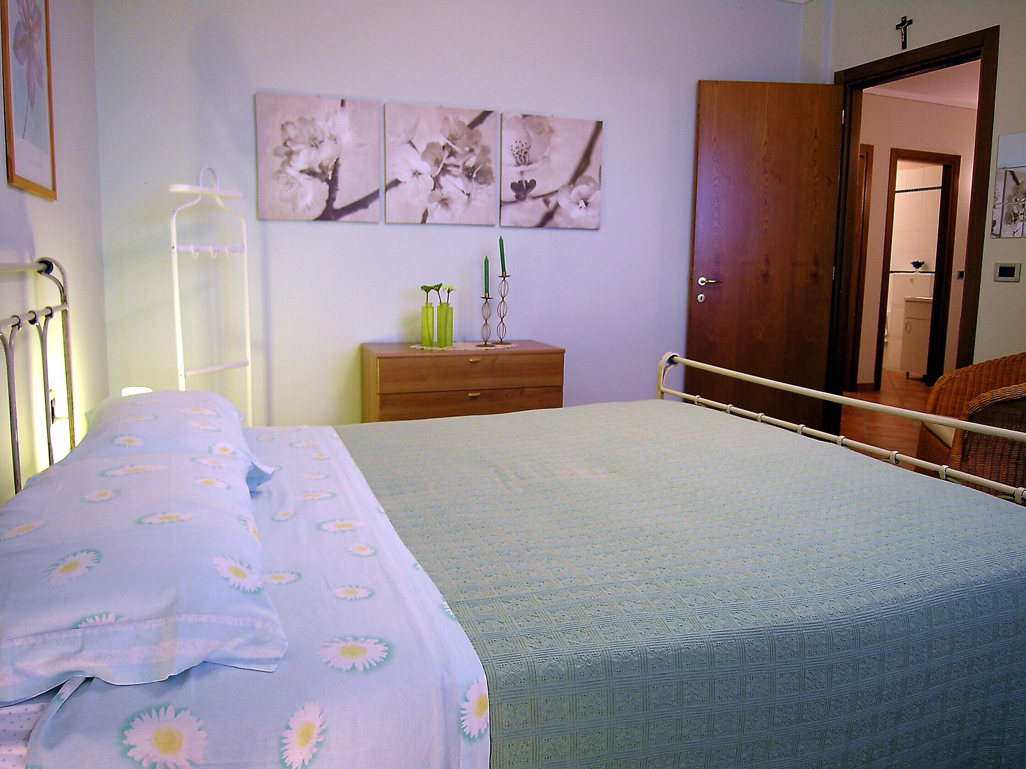 A bedroom with a bed, a nightstand, a wooden dresser, and a door leading to another room.