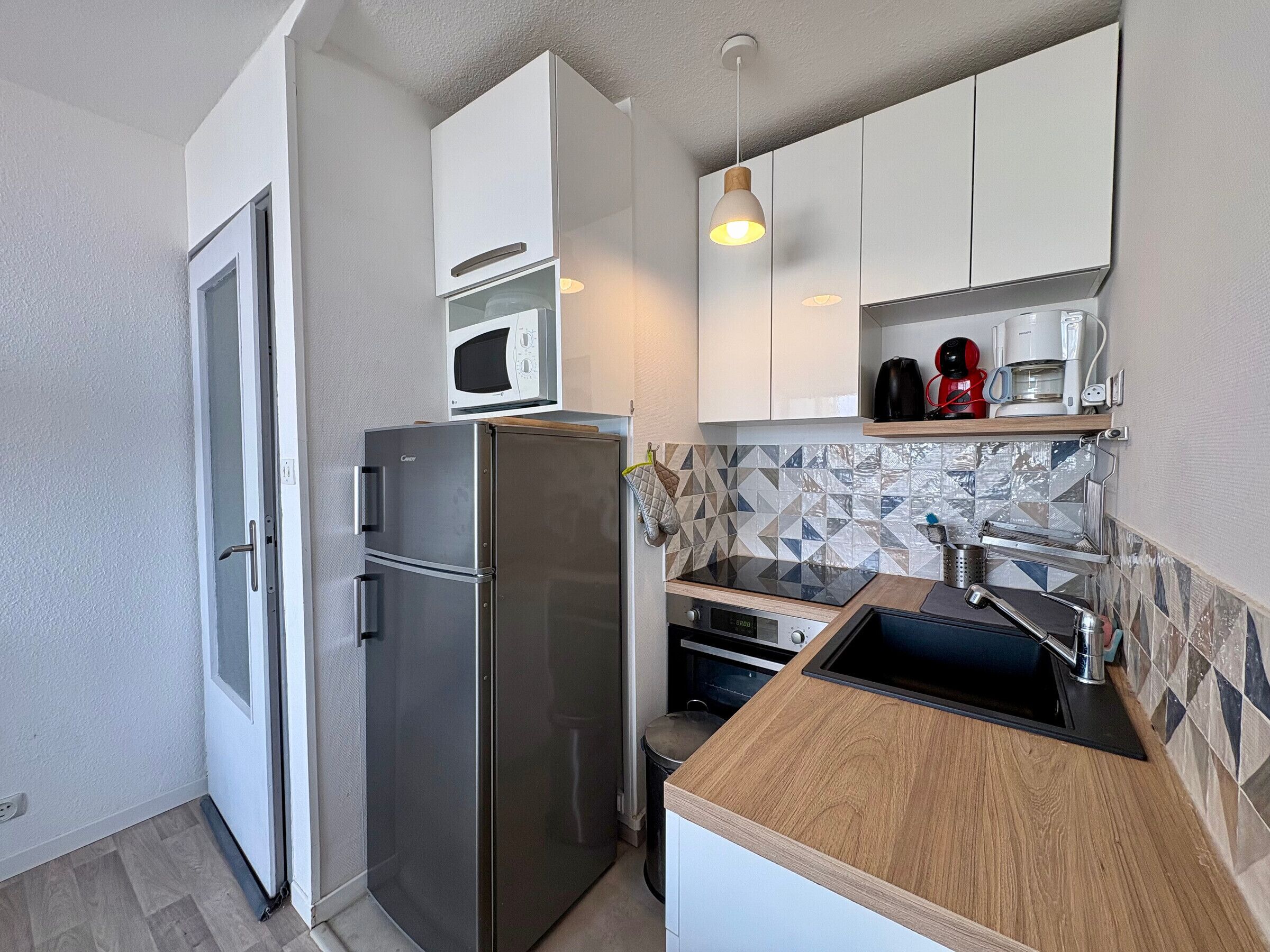 A compact kitchen with a refrigerator, microwave, oven, and a wooden countertop.
