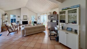 A spacious living area with a high ceiling, a sofa, chairs, a TV, and a cabinet with glassware. - Spacious House with Garden, Terrace, Near Forest and Beach - Saint Jean de Monts (Saint-Jean-de-Monts)