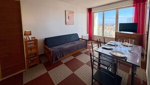 Un espacio habitable compacto con sofá, mesa de comedor, sillas, televisor y ventana con vista a la ciudad.