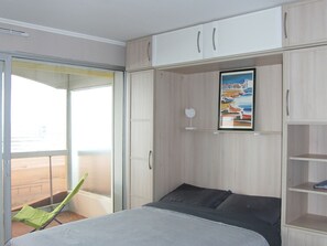 A bedroom with a bed, a green chair, a sliding door, and a painting on the wall. - Comfortable studio sea view with private parking (Saint-Jean-de-Monts)