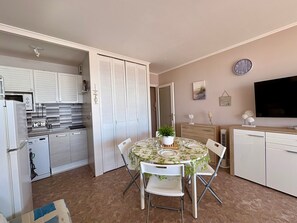 Una cocina compacta con armarios blancos, un microondas y un comedor con una mesa dispuesta para dos.