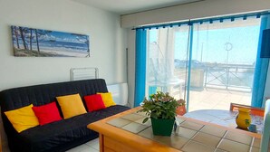 A room with a black sofa, a wooden table, a green plant, and a painting on the wall.