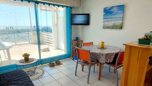 A room with a balcony, a TV mounted on the wall, a dining table with chairs, and a bed.