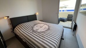 A hotel room with a bed, a nightstand, a lamp, and a view of the outside balcony. - Beautiful T2 with large terrace and parking, near the sea (Valras-Plage)