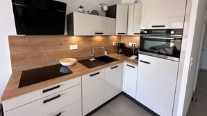 A modern kitchen with white cabinets, a wooden countertop, a black sink, and a built-in oven. - Beautiful T2 with large terrace and parking, near the sea (Valras-Plage)
