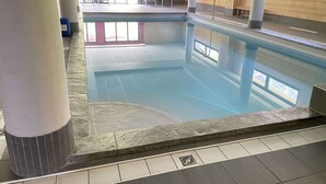 An indoor swimming pool with clear water, tiled flooring, and wooden walls.