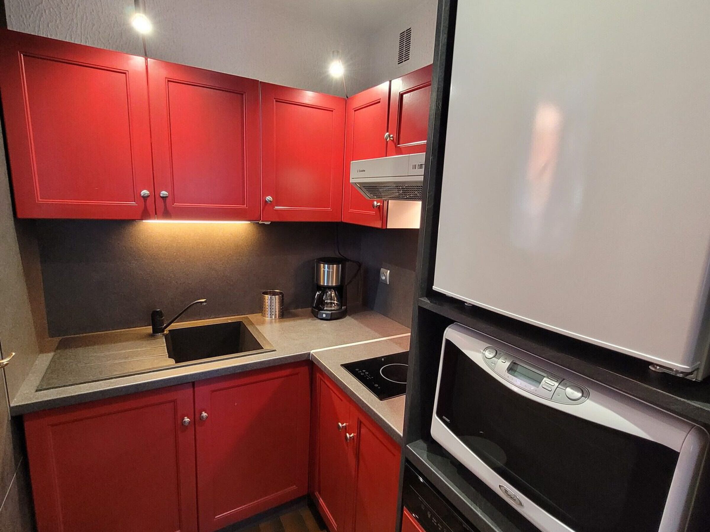 Une cuisine de taille réduite avec des meubles rouges, un évier, une machine à café et un four à micro-ondes.
