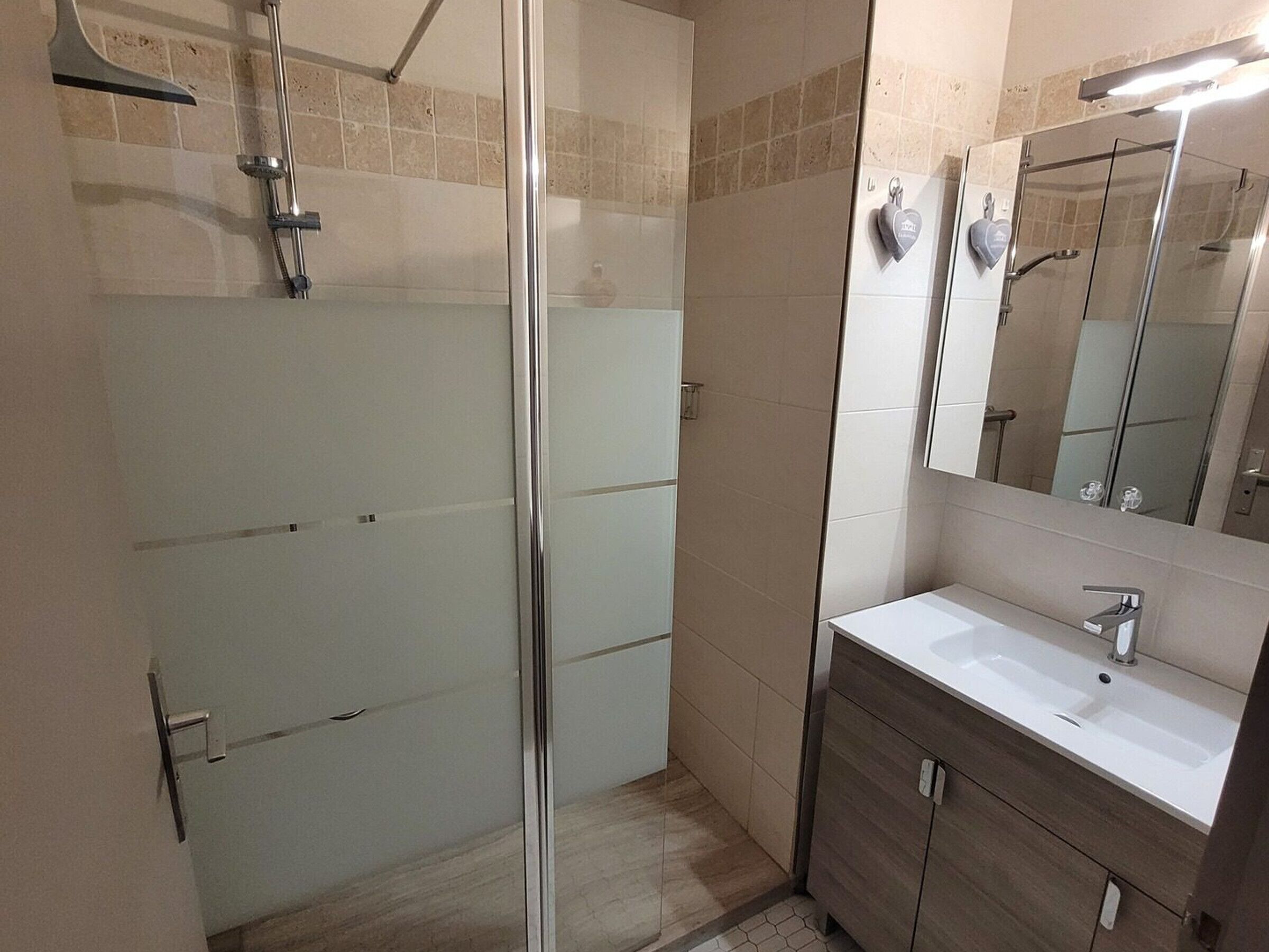 Une salle de bain moderne avec une douche à l’italienne en verre, un lavabo blanc et un meuble-lavabo en bois.