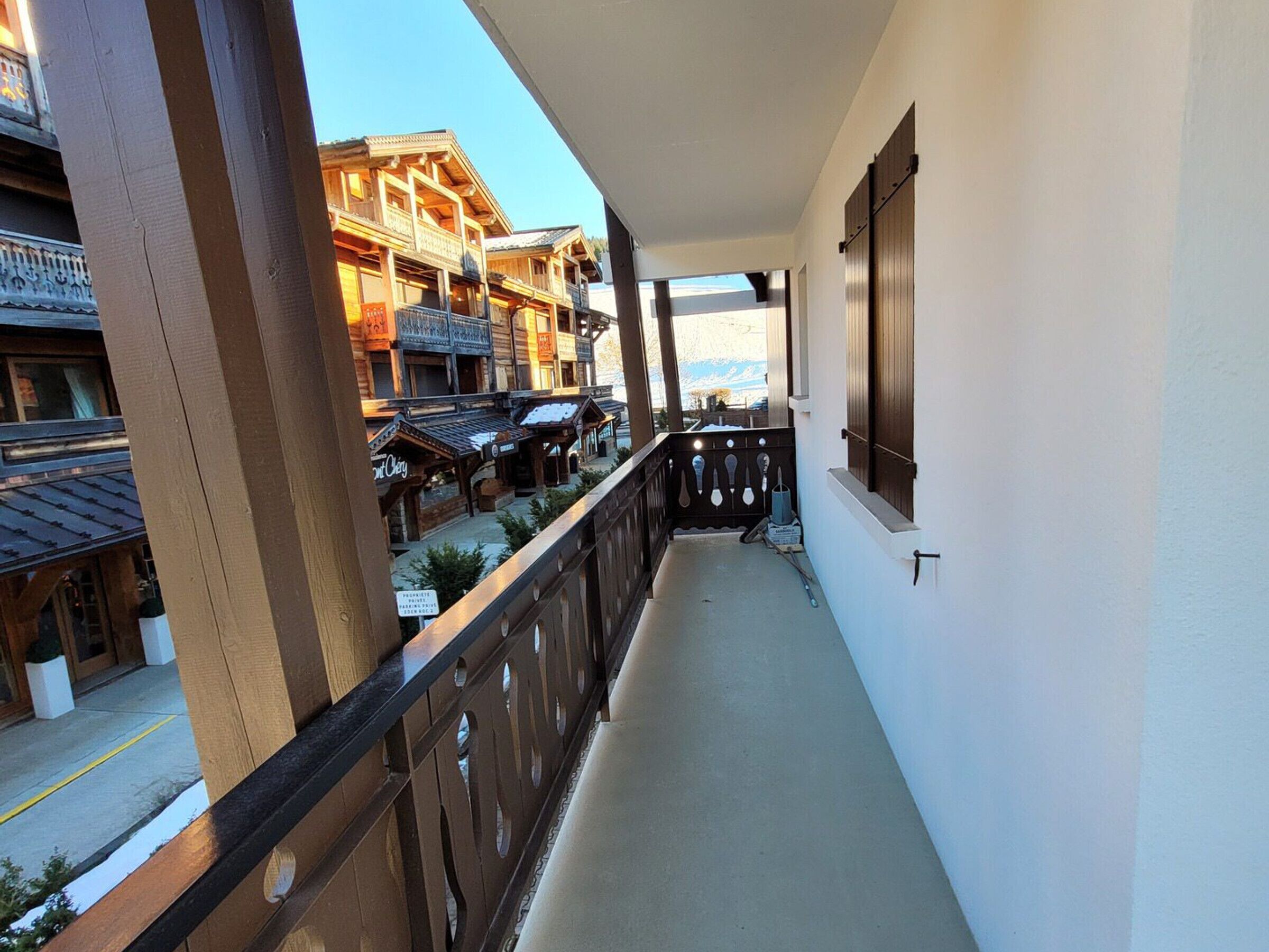 A balcony with a view of traditional wooden buildings, a railing, and a window with blinds.