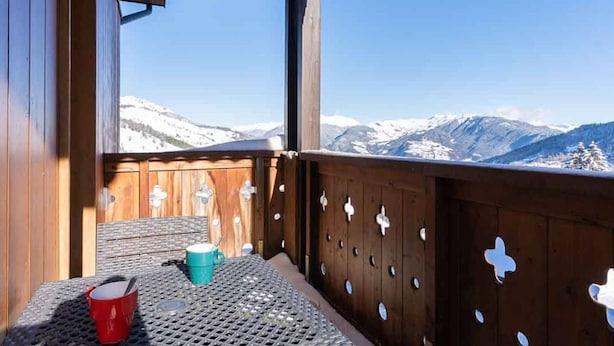 A wooden balcony with a metal table and chairs, a red mug, and a blue mug.