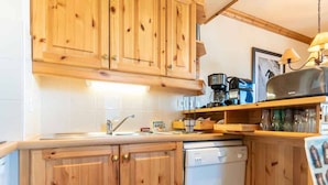 A compact kitchen with wooden cabinets, a dishwasher, a coffee maker, and a trash bin.