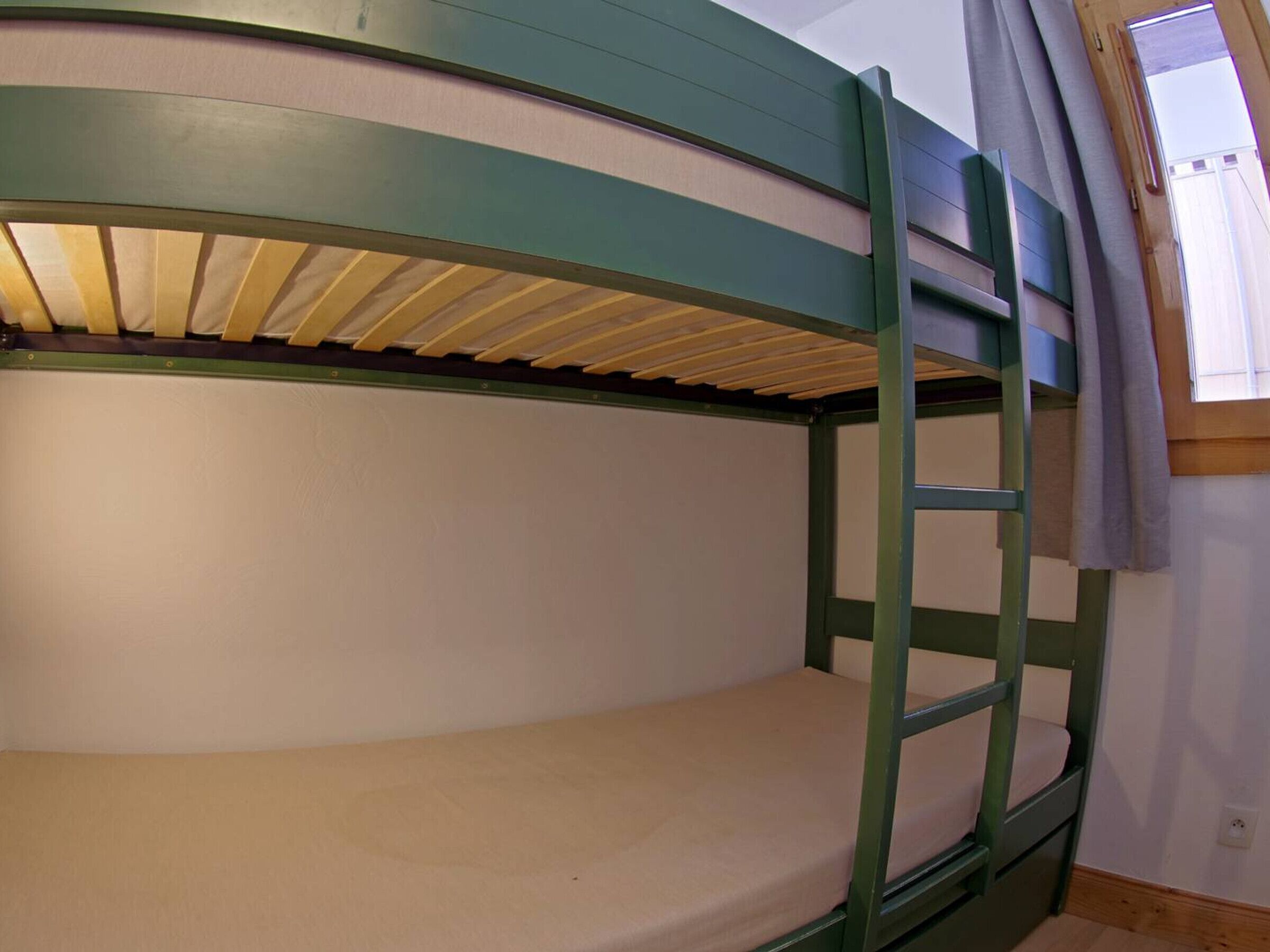 A bunk bed with a ladder, a window with curtains, and a white wall.