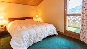 A bedroom with a wooden ceiling, a large bed, two bedside lamps, and a window with a view of the outdoors.
