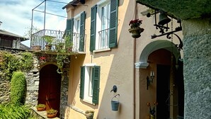 A two-story building with green shutters, a stone facade, and a balcony with plants.