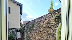A window view of a stone wall, two potted plants, and a jar of colorful candies on a windowsill.