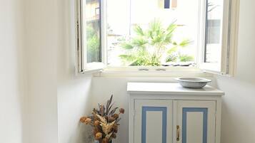 A bathroom with a window, a white stool, a cabinet, and a toilet.