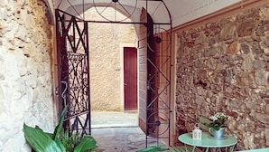 A stone-walled corridor with a metal gate, a potted plant, and a small round table with a chair.