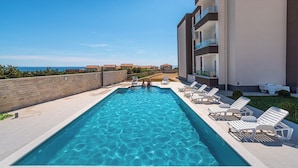 A swimming pool with lounge chairs, a view of the sea, and a building with balconies. - Deluxe Villa Laura With Pool Studio 1b (Novalja)
