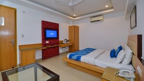 A hotel room with a bed, a desk, a glass-top table, a television, and a ceiling fan. - Hotel White Pearl (New Delhi)