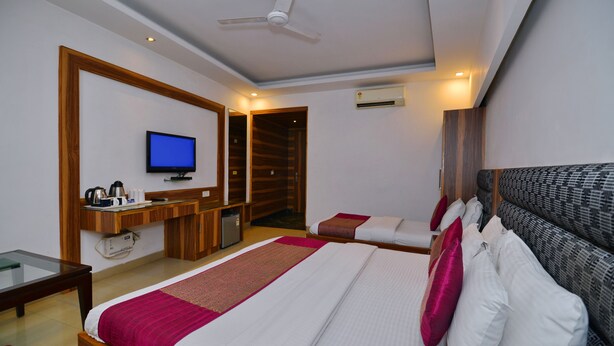 A hotel room with a bed, a desk, a television, and an air conditioning unit. - Hotel White Pearl (New Delhi)