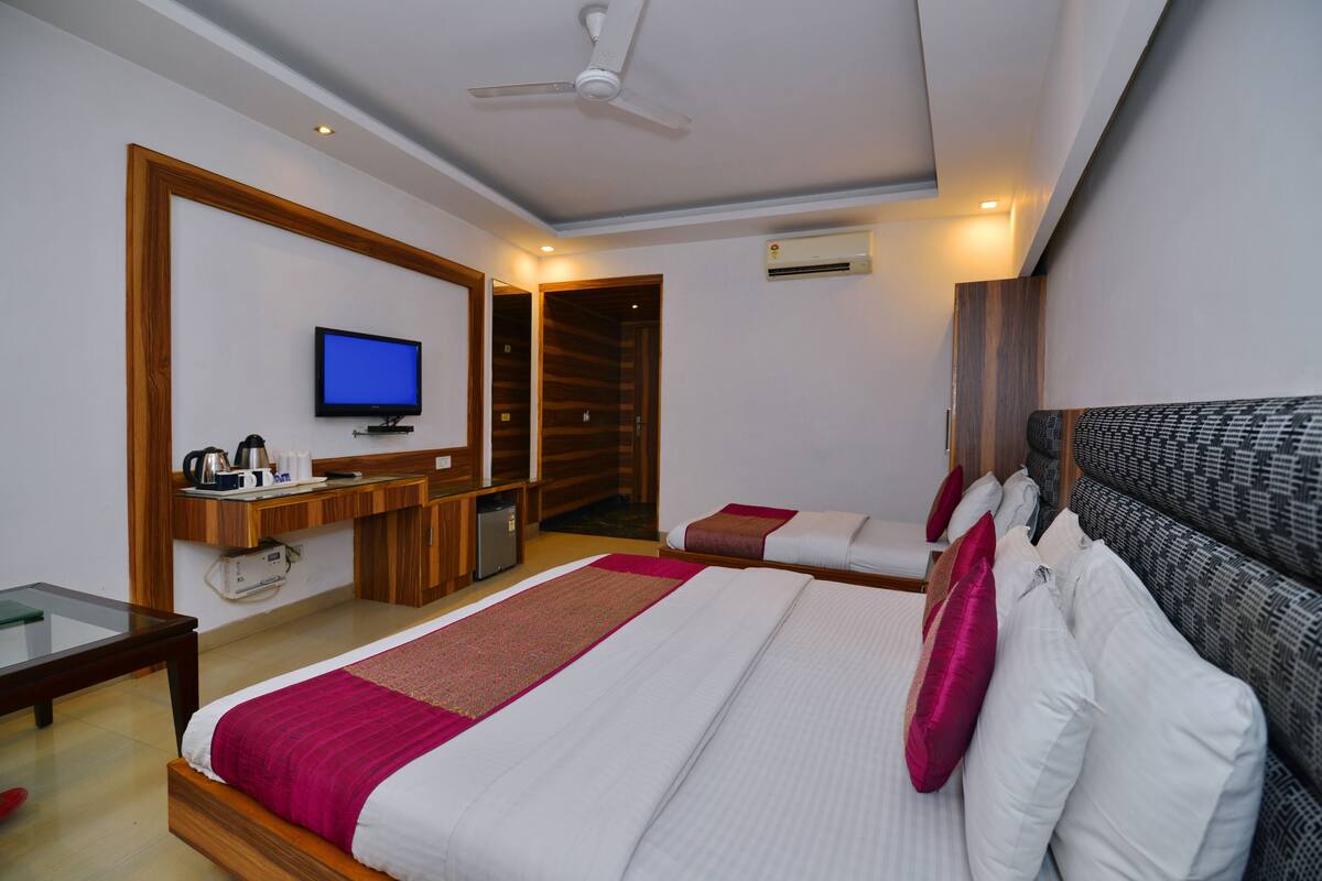 A hotel room with a bed, a desk, a television, and an air conditioning unit.