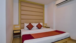 A neatly made bed with a wooden headboard, two bedside tables, and a red blanket. - Hotel White Pearl (New Delhi)