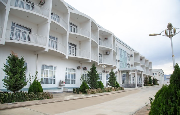A multi-story hotel with balconies, air conditioning units, and a street in front. - Ussat Hotel (Ashgabat)