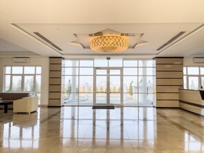 Een ruime lobby met een grote kroonluchter, een receptiebalie en uitzicht buiten door grote ramen.