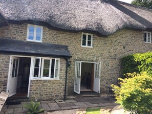 A stone house with a thatched roof, two open doors, and a small garden area with a bench. - Stunning 3-bed Cottage in Dorchester (Dorchester)